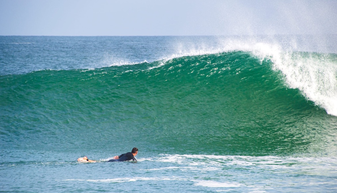Surfeur à la rame devant une vague qui se creuse