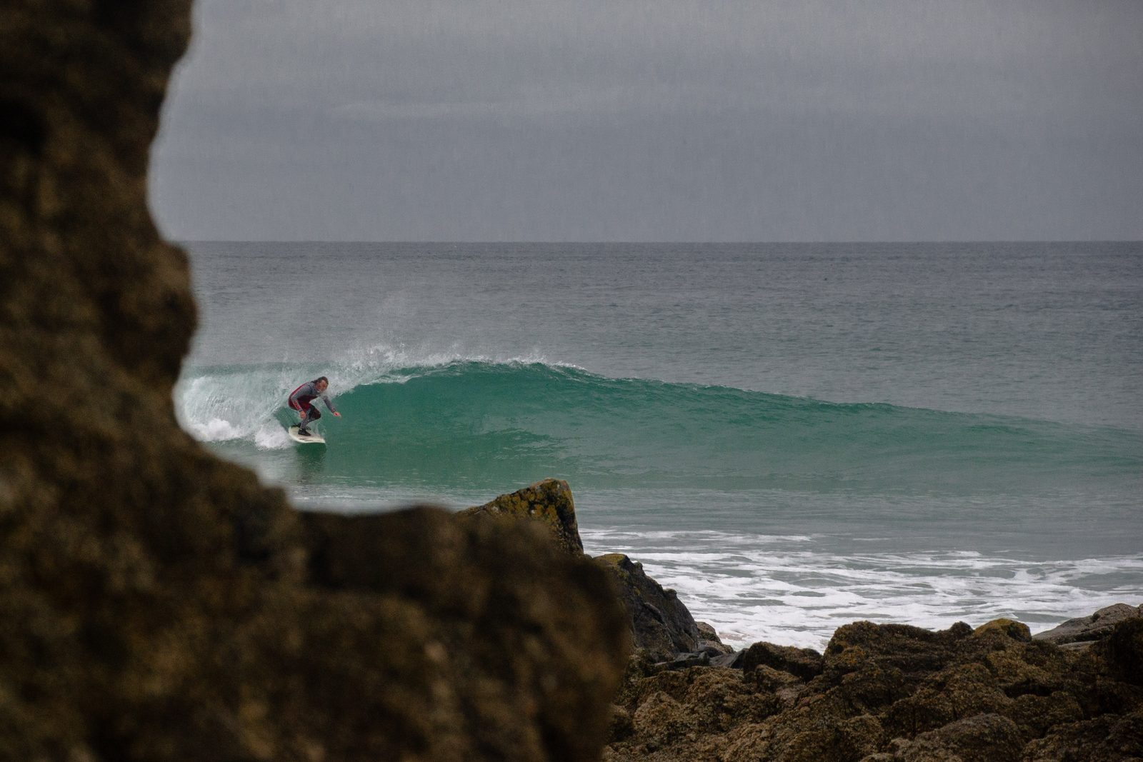 Surfeur sur une vague, vu entre les rochers