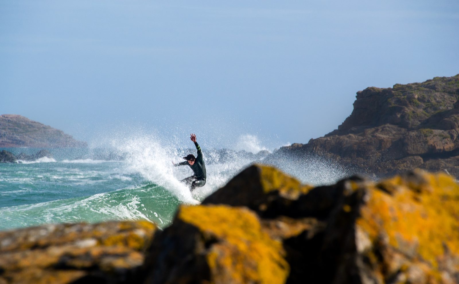 Surfeur en plein virage derrière des rochers couverts de lichen