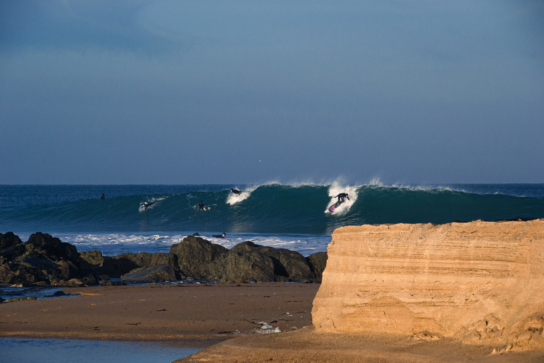 Surfeurs au line-up derrière les rochers et une falaise de sable